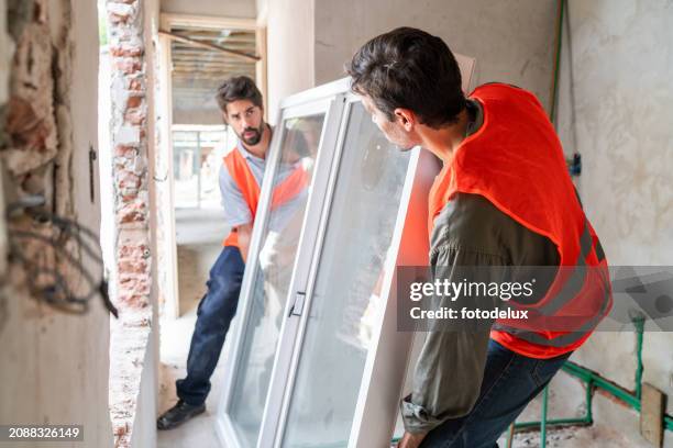 des travailleurs de la construction installent une nouvelle fenêtre dans un bâtiment - remplacement photos et images de collection