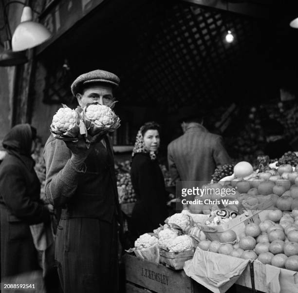 Shopper holds up two cauliflowers on a grocer's stall, where some prices are controlled by the Ministry of Food as rationing persists after the...