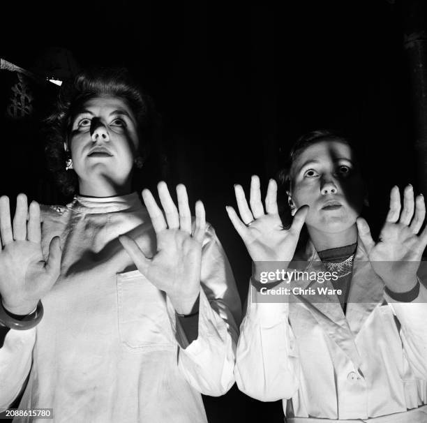 Iris Brown and Beryl Wilkey, both disciples of Reverend Harold Nicholson, whom Nicholson has also cured, raise their hands during a faith healing...