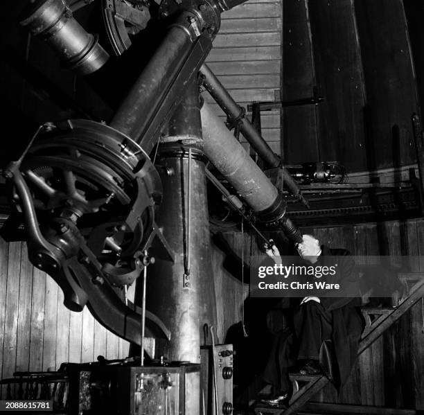 Man in a clerical collar peering through the eyepiece of a large telescope in an observatory, 1948.