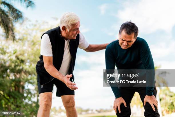hombre maduro cansado hablando con un amigo después de correr por el parque público - sin aliento fotografías e imágenes de stock
