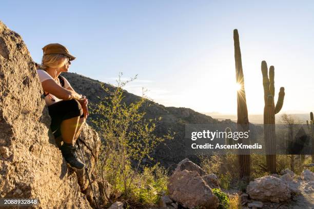 reife frau hält auf felsen über wüste inne - arizona stock-fotos und bilder