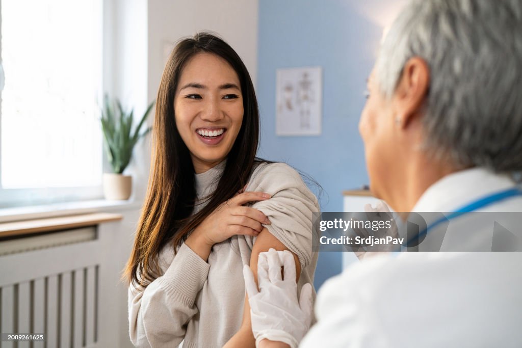 Senior Caucasian female doctor giving an flu vaccine to a female patient Japanese ethnicity