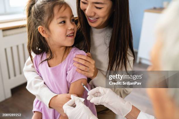 Brave Japanese girl receiving a vaccine from a senior female Caucasian pediatrician