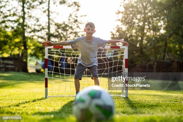 the boy plays football in the meadow, stands on the goal to defend the goal - international team soccer stock pictures, royalty-free photos & images