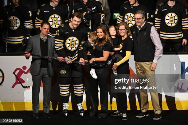 Jmes van Riemsdyk of the Boston Bruins, accompanied by his family, receives a silver hockey stick from general manager Don Sweeney for playing 1,000...
