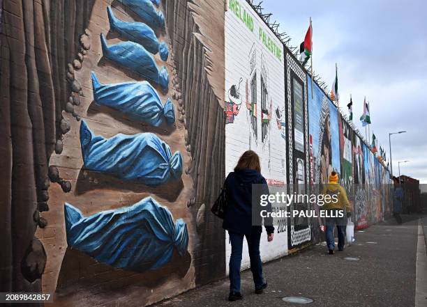 Pedestrians walk past a mural painted in solidarity with the people of Palestine, on the International Wall on the Falls Road in Belfast, Northern...