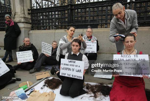 Protesters hold signs against the plight of people living in Gaza while their colleagues have their heads shaved outside the Houses of Parliament on...