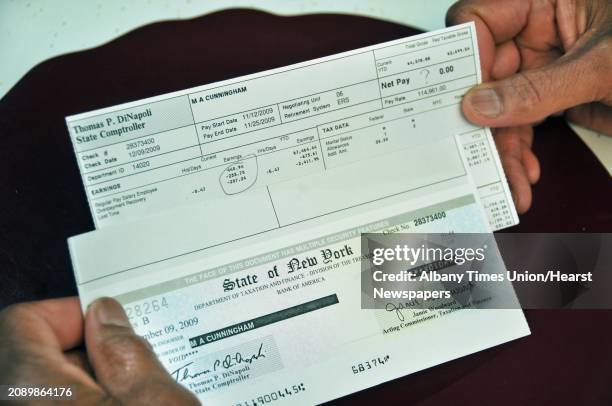 Mike Cunningham holds a NYS paycheck marked "VOID" and a pay stub for $0.00, in his Colonie home Wednesday March 31, 2010. Cunningham is a NYS Dept...