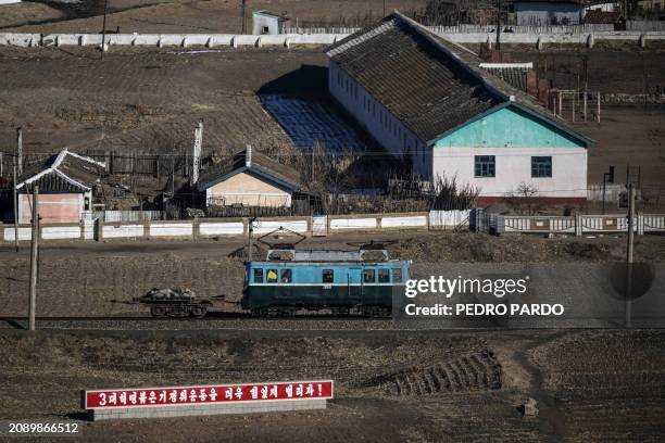 This picture taken on February 26, 2024 shows a mobile wagon passing by a sign reading, "Let's proactively promote the three generations of...