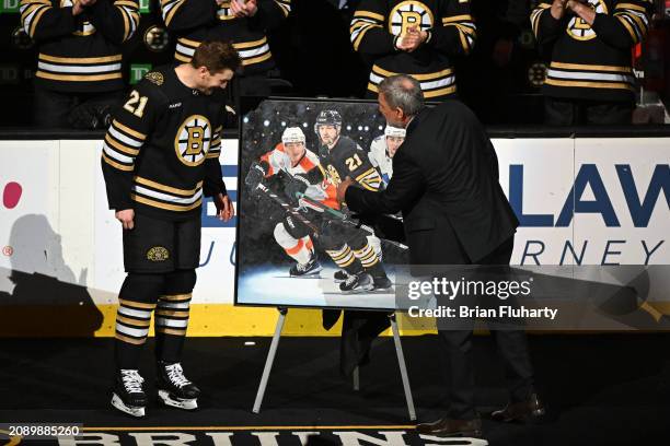 James van Riemsdyk of the Boston Bruins looks at a painting with president Cam Neely during a ceremony for playing in 1,000 NHL games before a game...