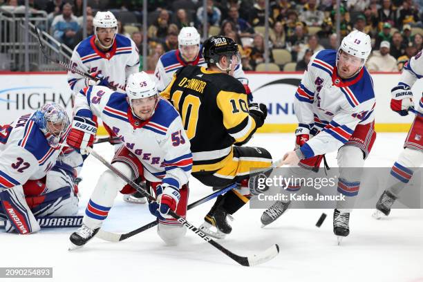 Drew O'Connor of the Pittsburgh Penguins gets tangled up with Ryan Lindgren and Alexis Lafreniere of the New York Rangers at PPG PAINTS Arena on...