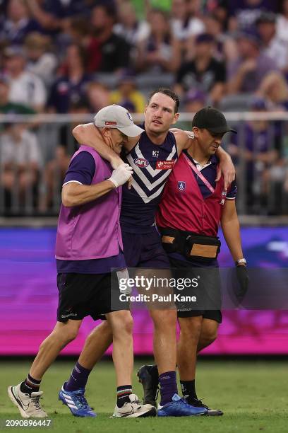 Brennan Cox of the Dockers is assisted from the field during the round one AFL match between Fremantle Dockers and Brisbane Lions at Optus Stadium,...