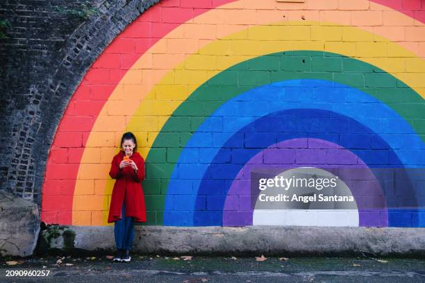 fashionable woman with phone standing before rainbow wall art - long coat stock pictures, royalty-free photos & images