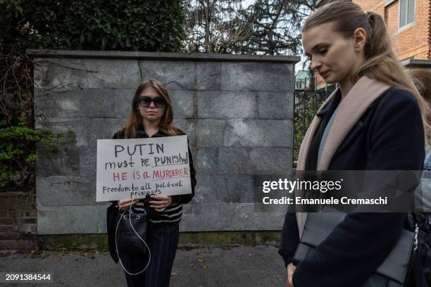 Russian dissident holds a placard against Vladimir Putin as she waits in line in front of the Russian consulate on March 17, 2024 in Milan, Italy....