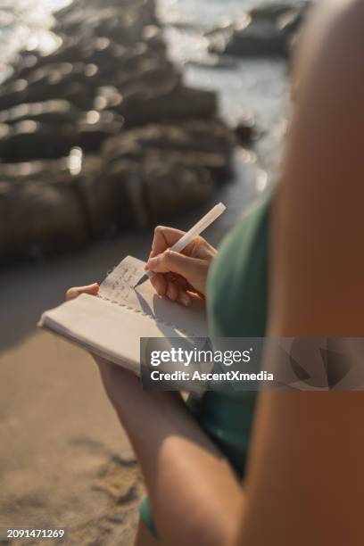 junge frau schreibt auf notizblock am strand - tagebuch stock-fotos und bilder