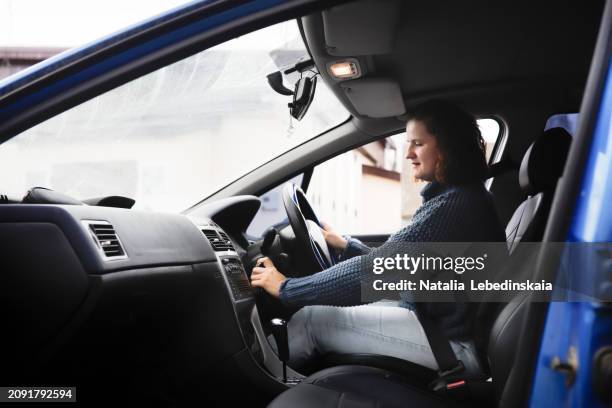 portrait of plus-size middle-aged woman in sweater turning on car engine, driving right-hand drive car - right hand drive stock pictures, royalty-free photos & images