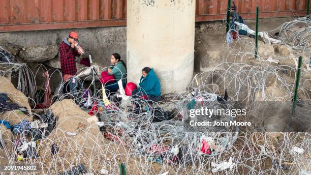 In an aerial view, immigrants wait under an international bridge after crossing the Rio Grande from Mexico and passing through coils of razor wire on...