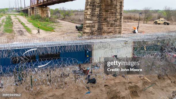 In an aerial view, a Texas National Guard soldier walks past a barrier of shipping containers and razor wire at he U.S.-Mexico border on March 17,...