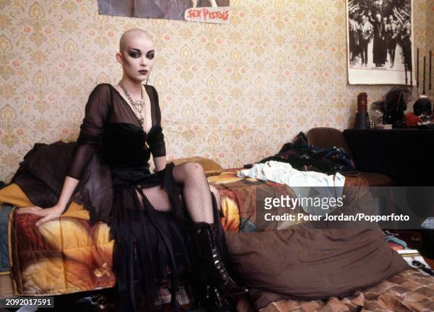 Punk with a shaved head in a bed-sit in London, circa 1983. On the wall are posters of Punk bands.