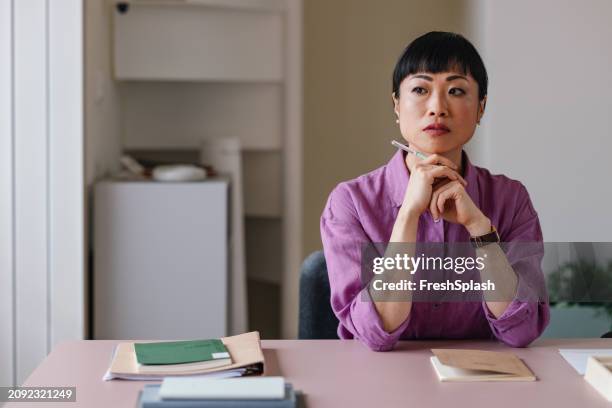 thoughtful professional woman contemplating at work desk - stern stock pictures, royalty-free photos & images
