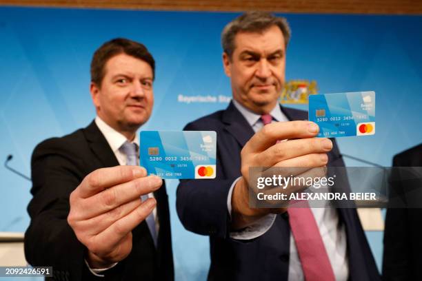 Bavaria's State Premier Markus Soeder and Bavaria's Secretary of State for the Interior Sandro Kirchner pose with a prepaid benefit card for asylum...