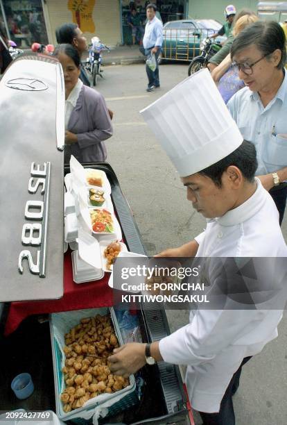 Thai food vendor sells lunch boxes out of the trunk of a Mercedes Benz 280 SE to attract customers on a street in Bangkok, 02 August 2001. Selling...