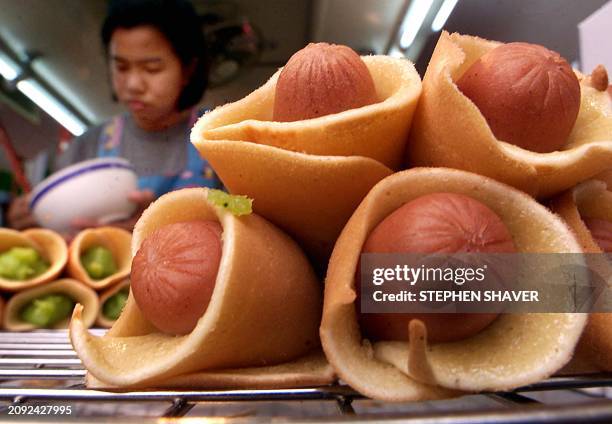 Woman prepares an assortment of snacks at her family's street-side food stall, including mini-dogs wrapped in light pancakes, in downtown Bangkok 17...