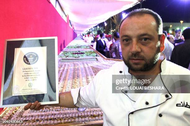 Syrian baker holds the certificate from the Guiness Book of World Records for a mosaic of traditional Arabic sweets, measuring 112 meters long, which...