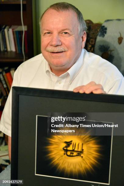 Paul Murray holds a symbol of the Baha'i faith, a framed Arabic calligraphic rendering known as "Greatest Name" at his home in Albany Thursday March...