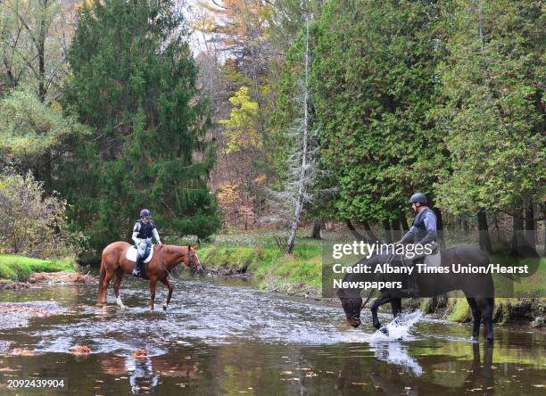 Ariston splashes in Geyser Brook as his rider Mike Rach, at right, of Ballston Lake and Carol Drake of Clifton Park, on Angie, stop to water the...
