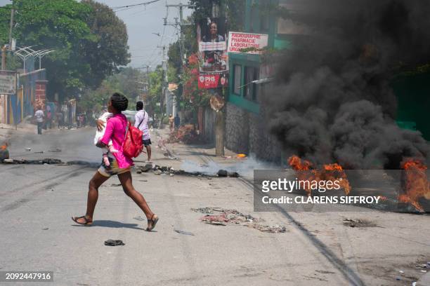 Woman carrying a child runs from the area after gunshots were heard in Port-au-Prince, Haiti, on March 20, 2024. Negotiations to form a transitional...