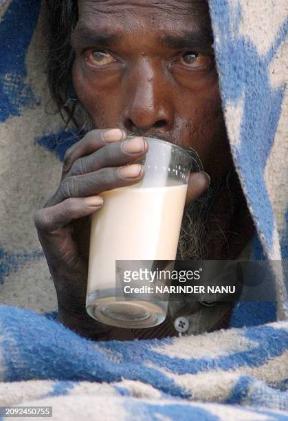 Indian beggar Subash drinks a glass of milk tea as he covers himself with a blanket to keep warm, in Amritsar, in India's northwestern state of...