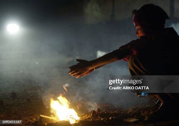 Young boy keeps warm on the street with the help of a fire, 13 December 2000 in New Delhi. Temperatures in the Indian capital are expected to reach a...