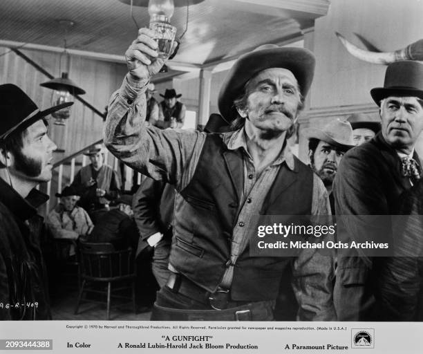 American actor and film director Kirk Douglas raises his glass in a busy saloon, in a scene from 'A Gunfight', filmed in Santa Fe, New Mexico, 1971....