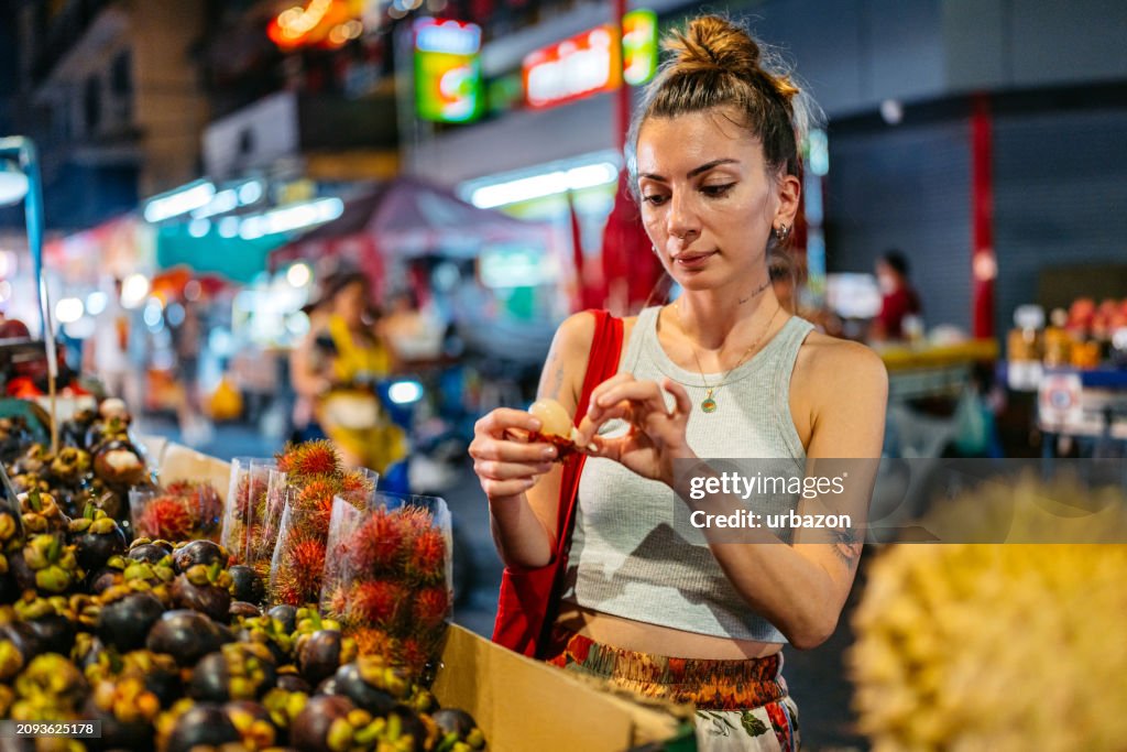 Young Female Tourist Eating Rambutan Fruit At The Night Market In Chinatown In Bangkok In Thailand