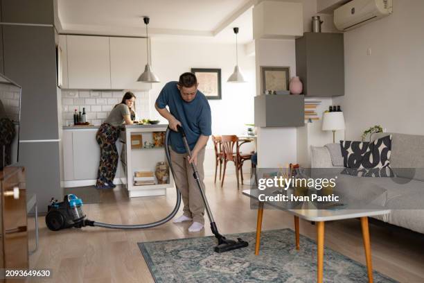 young man with special needs vacuuming carpet in the living room. - developmental disability stock pictures, royalty-free photos & images