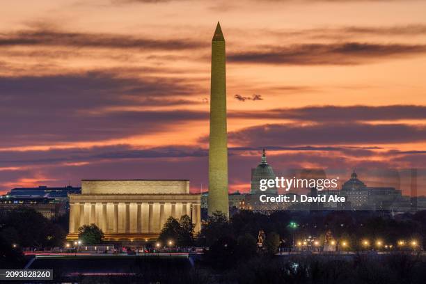 Sunrise turns the sky shades of orange behind the Lincoln Memorial, Washington Monument, and US Capitol Building on March 18 in Washington, DC.