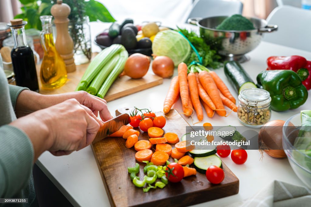 Close up of woman's hands slicing fresh organic carrots on kitchen counter