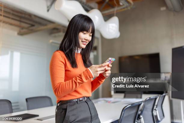 happy chinese young woman in office with mobile phone in conference room - employee mobile phone stock pictures, royalty-free photos & images