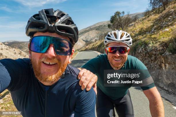 two mature cyclists (brothers) take a selfie as they climb a steep climb in the spanish mountains - frère photos et images de collection
