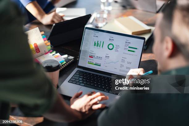 team analyzing data on laptop screen in busy workspace - marketing stock pictures, royalty-free photos & images
