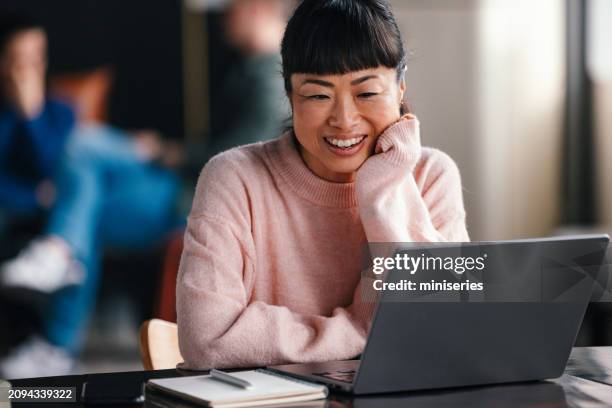 young woman smiling while working on laptop in co-working space - content stock pictures, royalty-free photos & images