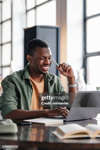 joven profesional que trabaja en una computadora portátil en un espacio de coworking - intensidad del color fotografías e imágenes de stock