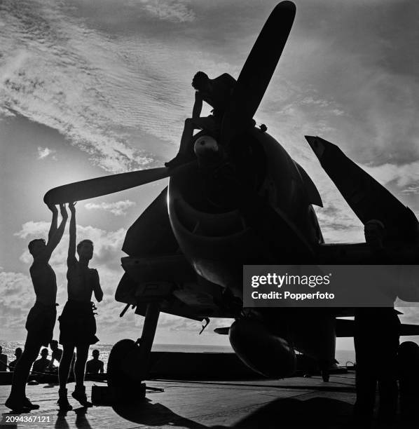Scene at sunset of maintenance ratings preparing a Fleet Air Arm Grumman F6F Hellcat fighter aircraft for an upcoming sortie on the flight deck of...