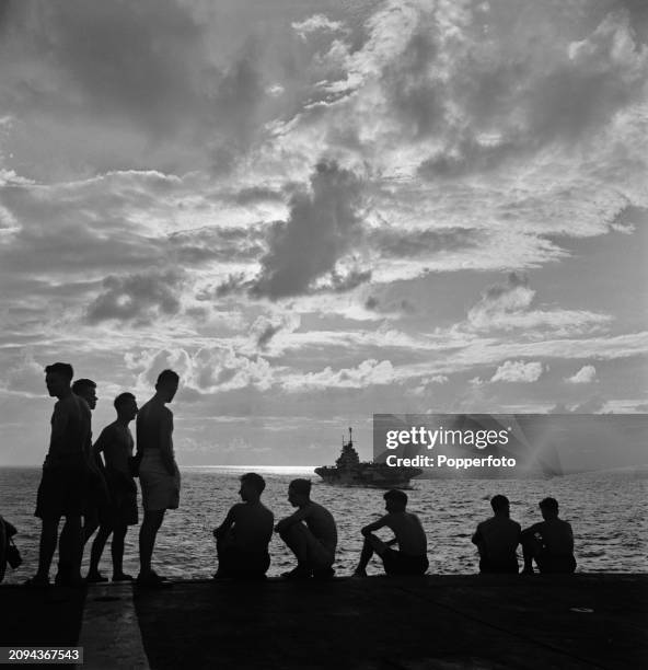 Scene at sunset of members of the crew observing a following sister ship from the flight deck of the Royal Navy Illustrious-class aircraft carrier...