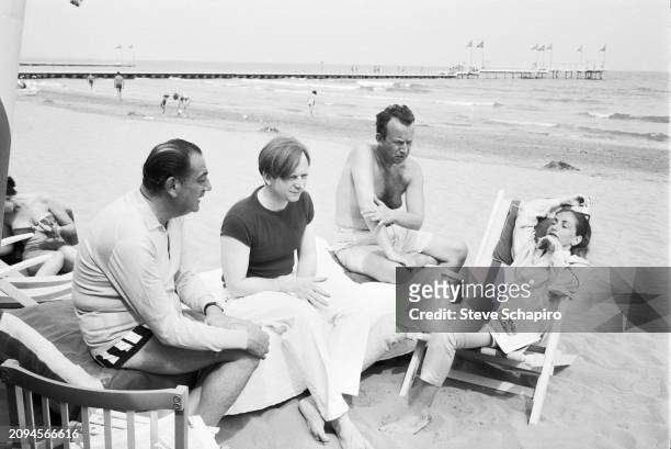 View of American author Tom Wolfe , with unidentified others, as they sits on the beach during the Venice Biennale, Venice, Italy, 1966.