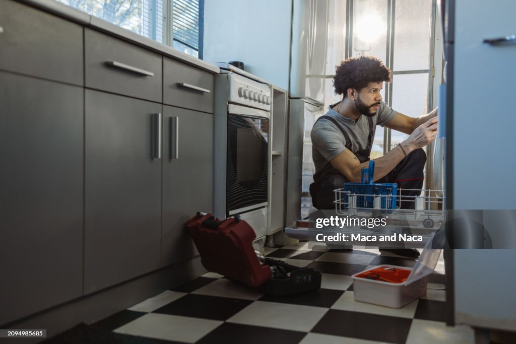 Un jeune bricoleur latin répare le lave-vaisselle dans la cuisine du client