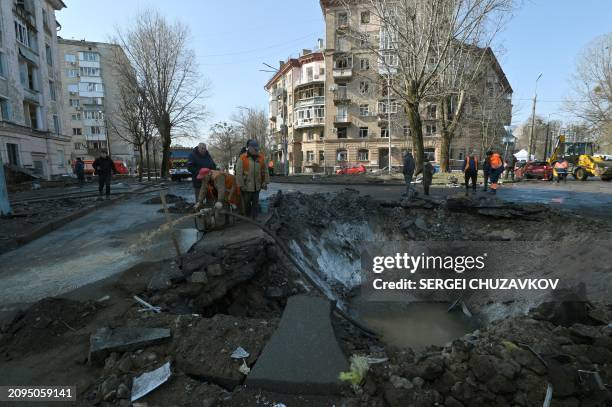 Ukranian municipal services workers survey and repair the damage following a missile attack in Kyiv, on March 21 amid the Russian invasion of Ukraine.