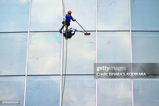 Janitor suspended on a cable cleans the glass facade of a hotel in Colombo on March 21, 2024.